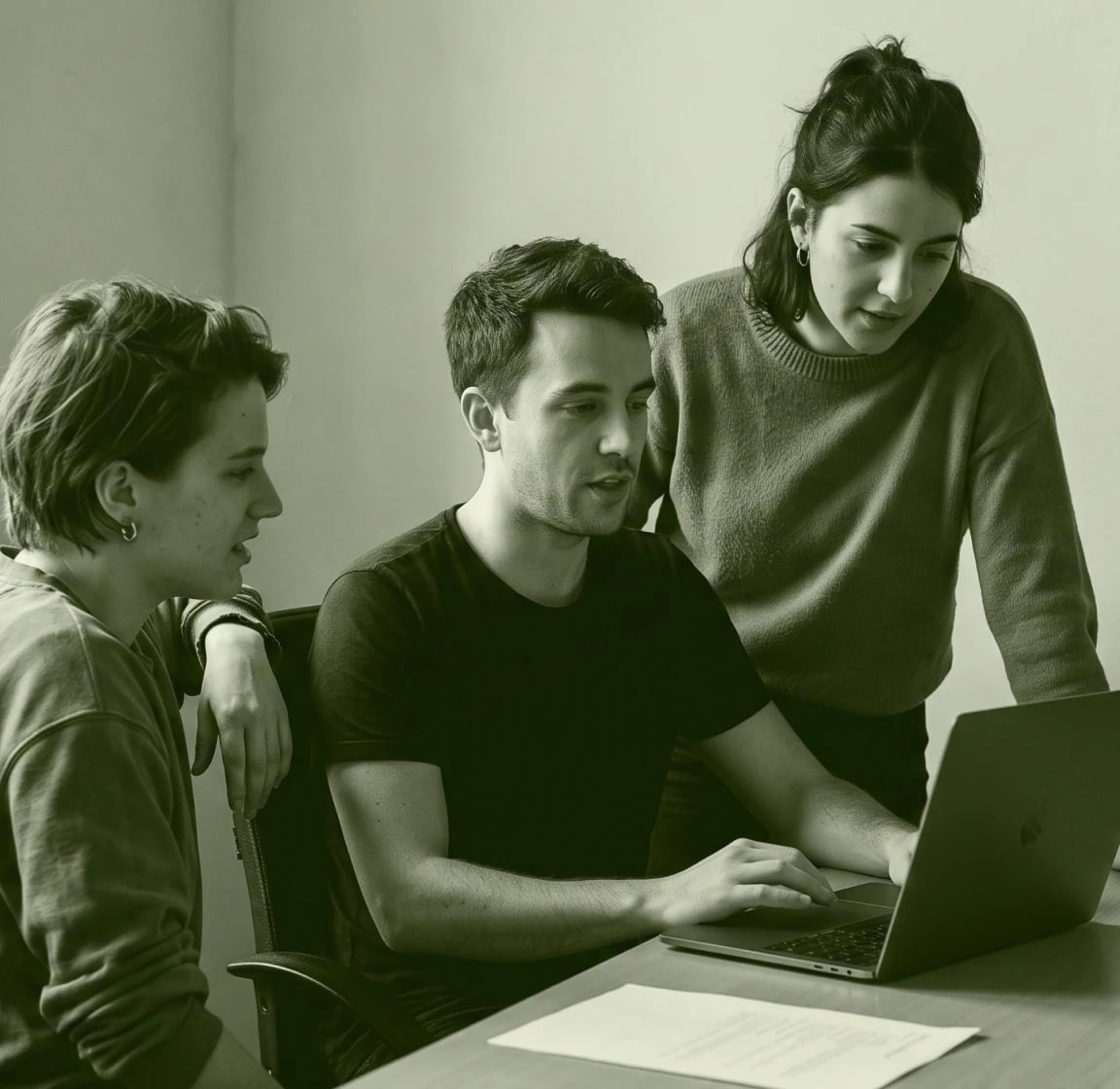 Three people gathered around a laptop at a table, in green duotone