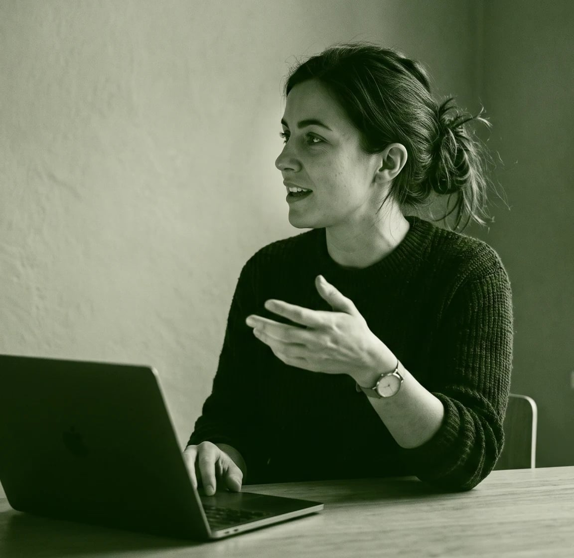 Person gesturing while speaking at a table, in green duotone